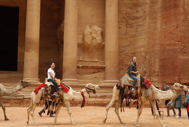 Students on camels in front of old ruins