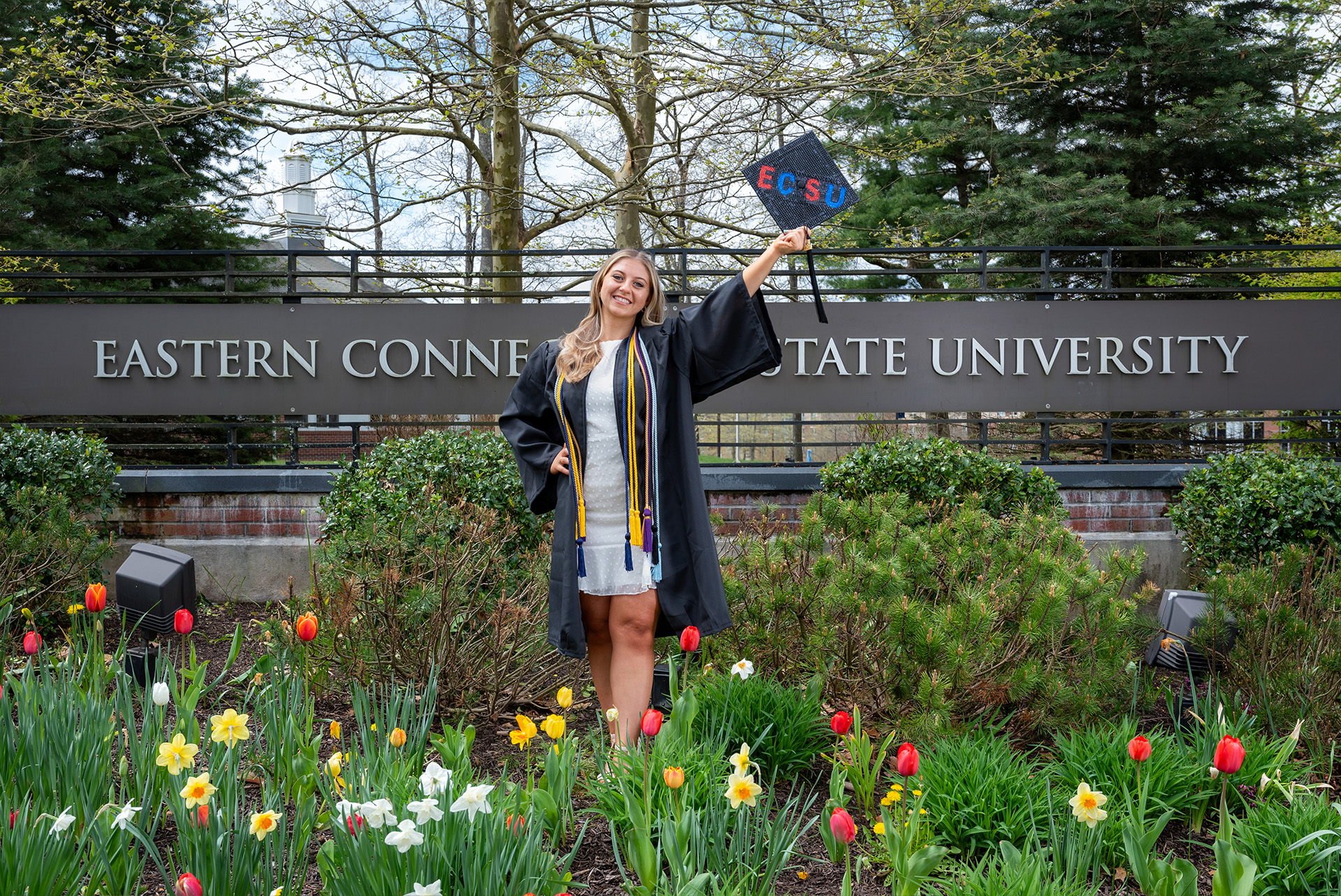 Student posing with diploma in front of Eastern's entrance sign