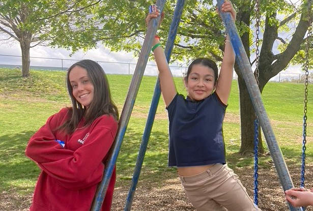student posing for photo with child holding on to swingset