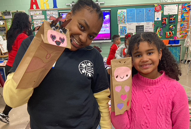 student and child holding paper bags decorated as puppets