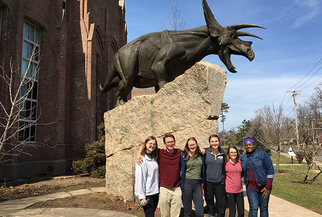 students posing on front of a statue of a dinosaur