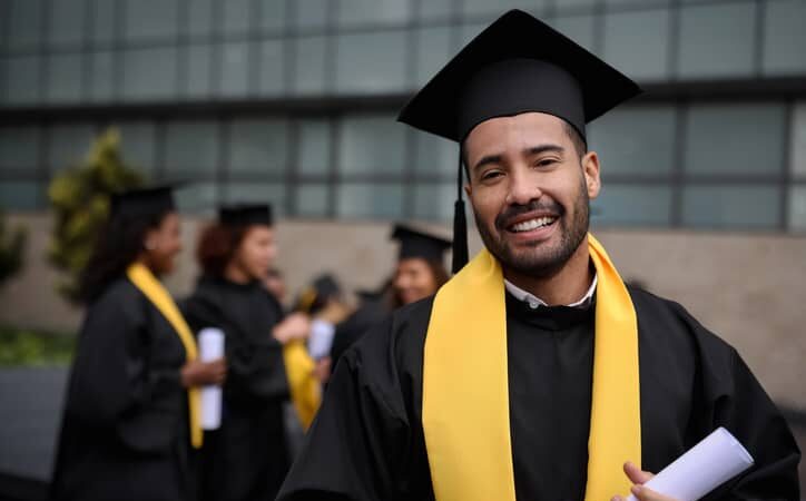 A happy male graduate student holding his diploma on graduation day.