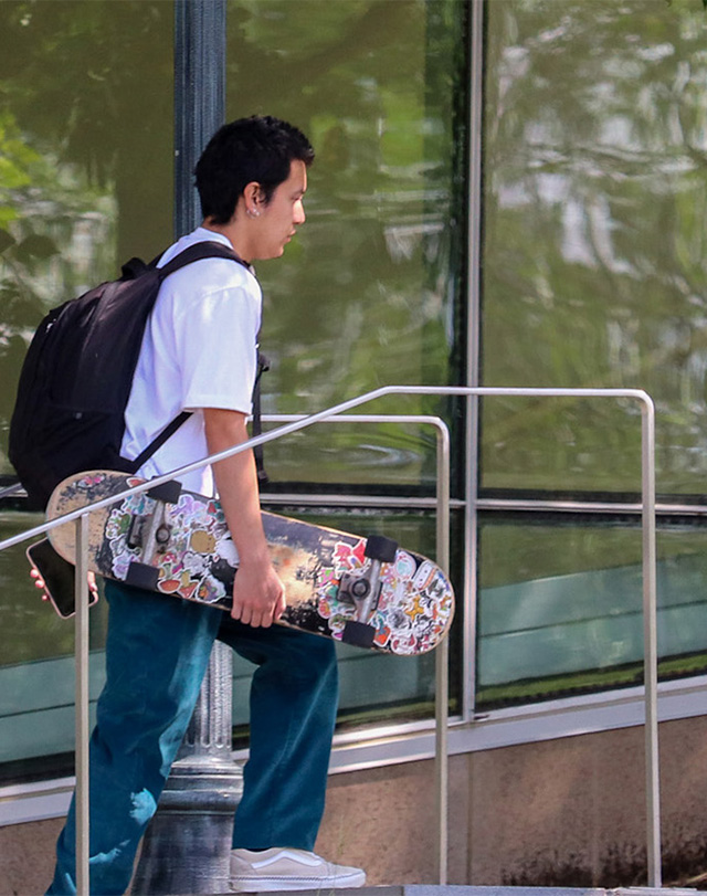 student walking past the Fine Arts Instructional Center with a skateboard